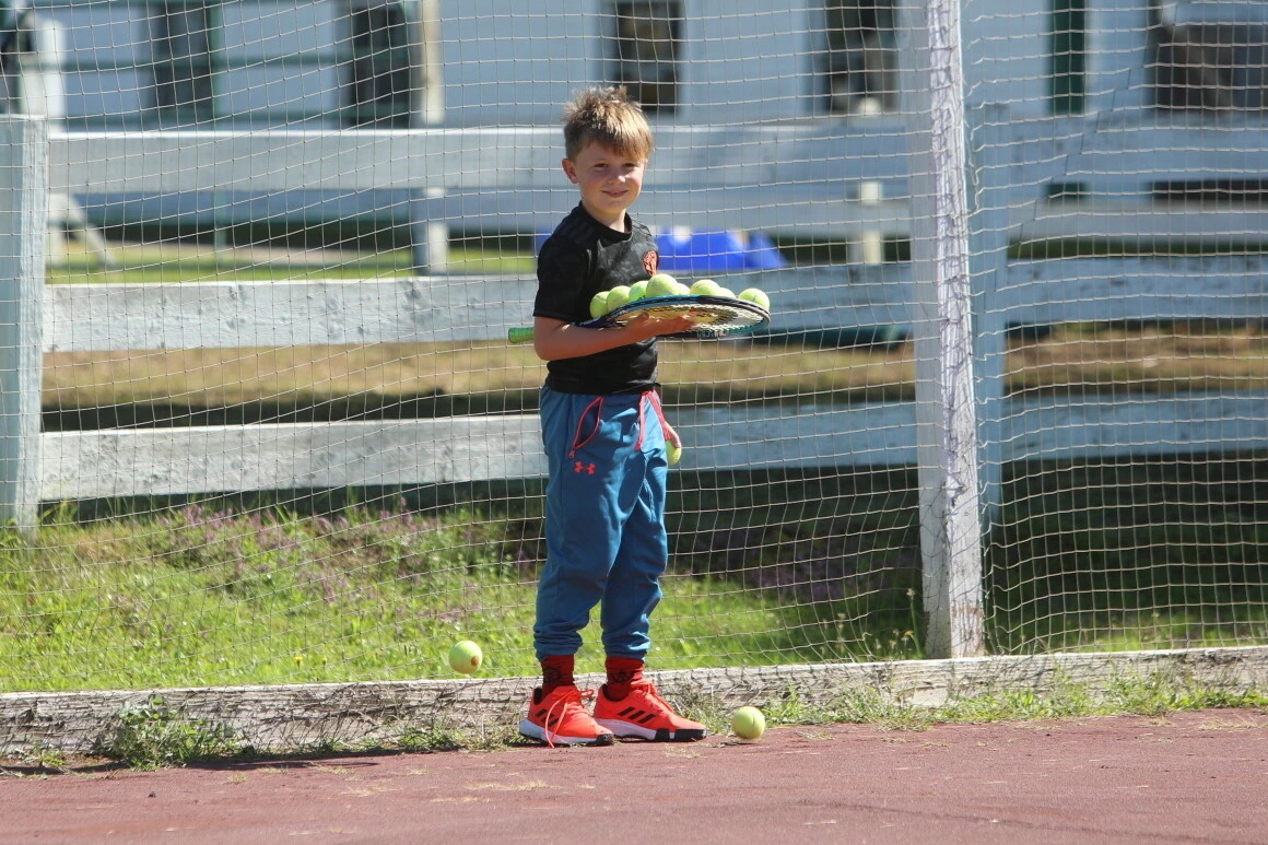 Young boy holding a basket full of balls on a clay court at Windridge tennis camp in Vermont